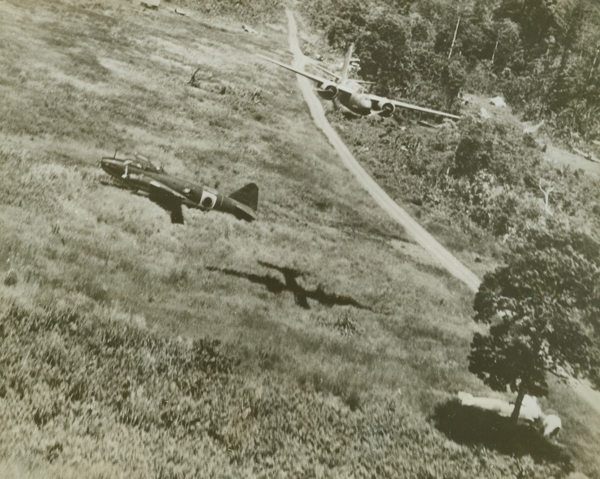 American Bomber Wallops Jap Planes, 2/2/1943. New Guinea – An American A-20 skims mere 100 feet above the ground at Lae, New Guinea, in a strafing attack on Jap planes.  It is passing over a disabled enemy bomber that will never fly again.  Under the tree (right), rests a Jap zero which has received its quota of American lead while another zero (edge of clearing, upper right) also will never see action again.  Two more enemy aircraft are near house (top center).Credit (U.S. Army Air Corps photo – ACME);