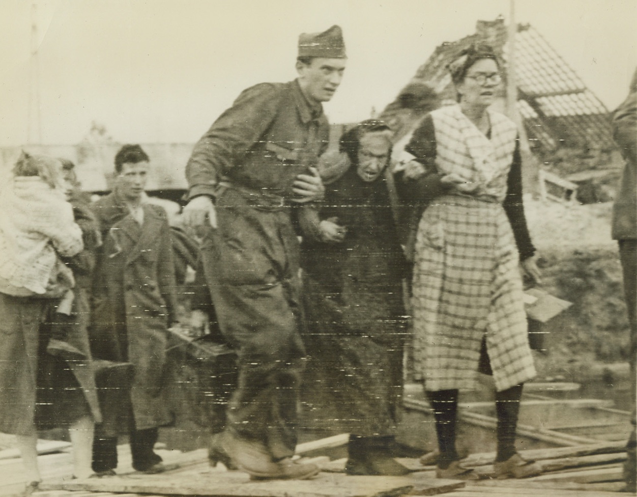 EVACUATION UNDER THE WHITE FLAG, 10/2/1944. CALAIS, FRANCE – With the guns of war temporarily silenced, an aged woman of Calais makes her way from that city during the 24-hour truce.  An FFI man and a Red Cross volunteer help her to cross Calais canal.  Shortly after the truce ended, Canadian troops captured the city.Credit: Acme photo via Army radio telephoto;