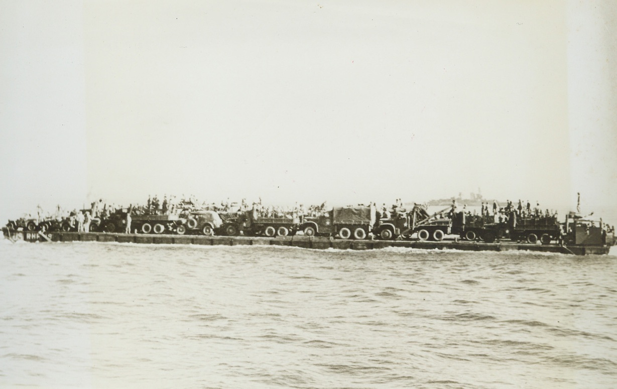 “RHINO FERRY” FOR INVASION FORCES, 6/6/1944. The most difficult phase of the initial operation against the European Continent—that of bridging the last few hundred yards between vessels and the beach—is being accomplished to a large degree through the use of the U.S. Navy’s modern pontoon gear. Made up of hollow boxes of welded metal, in two sizes, a huge, self-propelled barge, called the “rhino ferry” can be put together aboard ship. When the objective is reached, sections of the raft can be lowered over the side, fastened into the whole with bolt, nuts, links, and angles. The, the “ferry” is ready to float vehicles and supplies ashore. The new style pontoons—or tanks—are built in two sizes, five by seven by five feet deep, and the other, seven by seven by five with one edge curved to serve as the prow of a barge. These rafts as a whole—or in sections—can be filled with water and used as piers or docks. Designed by Capt. John N. Laycock, Civil Engineer Corps, USN, Washing, D.C., these pontoons have been used previously in invasions of Attu, Africa, Sicily, and Italy. I this series of photos, the “rhino ferry” is shown being assembled and put to use.  NEW YORK BUREAU Loaded with motor vehicles, the “rhino ferry” heads for the beach from a transport. Credit: U.S. Navy photo from Acm;