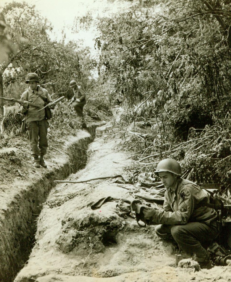 Captured Nazi Trench Near St. Lo, 7/20/1944. France -- Sgt. Thomas McMullen (foreground) of Maplewood, N.J., and Cpl. Leonard Redeyoff, Philadelphia, Pa., examine Nazi defenses in a trench hidden by a hedge in the St. Lo. sector of France. Trench was taken by Yank troops after bitter Nazi resistance had been quelled. Hedgerows around St. Lo provide perfect cover and makes it easy for the Germans to defend any given area. 7/20/44 (ACME);