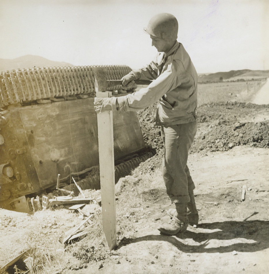 SAFETY POSTS FOR ITALIAN ROADS. Pvt. Omero Del Papa of Galveston, Texas, drives a safety post into the edge of an Italian road, next to an overturned German tank.;