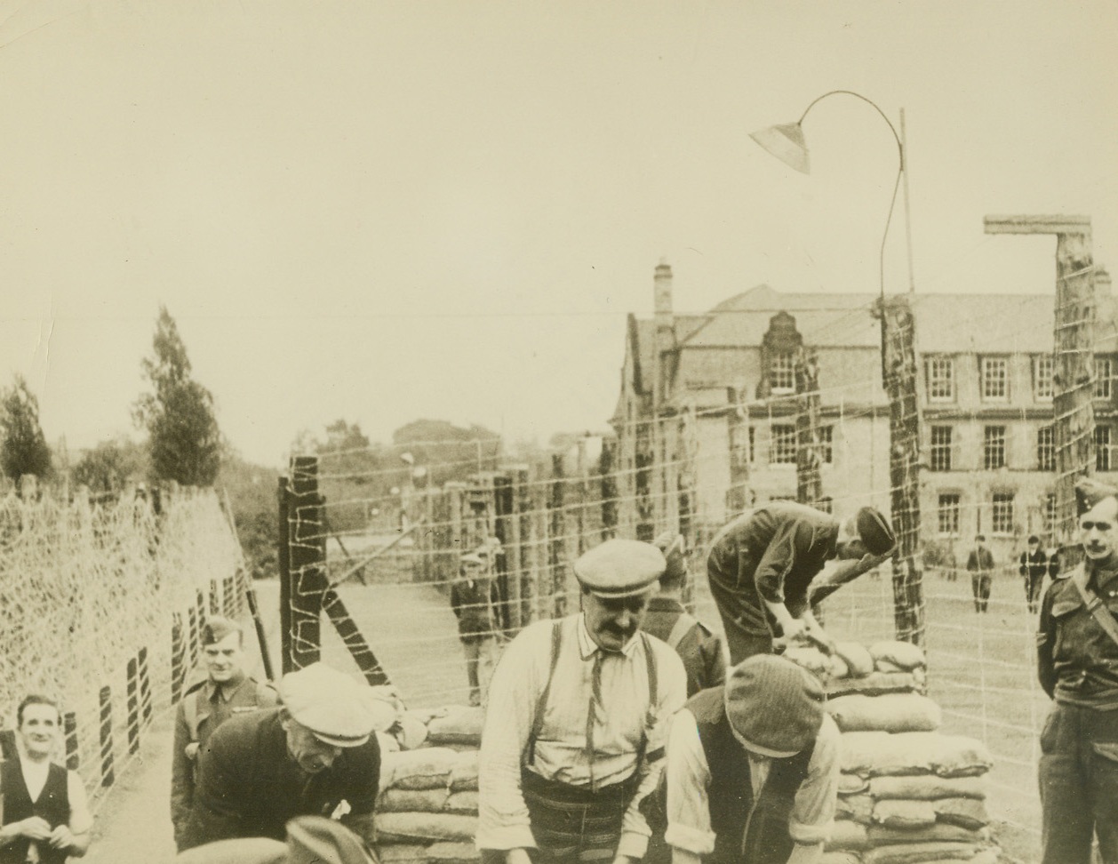 Air Raid Shelter for German Prisoners of War, 11/9/1939. Somewhere in England – While workmen in the foreground build an air raid shelter for their protection in case German bombers should drop their “eggs” in the vicinity, German prisoners of war can be seen exercising on the grounds of a large country mansion where they are interned for the duration. This picture, one of the first to be made of German war prisoners, who included members of German U-Boat crews, was rushed to the United States via Trans-Atlantic Clipper. Passed by Censor. Credit: ACME;